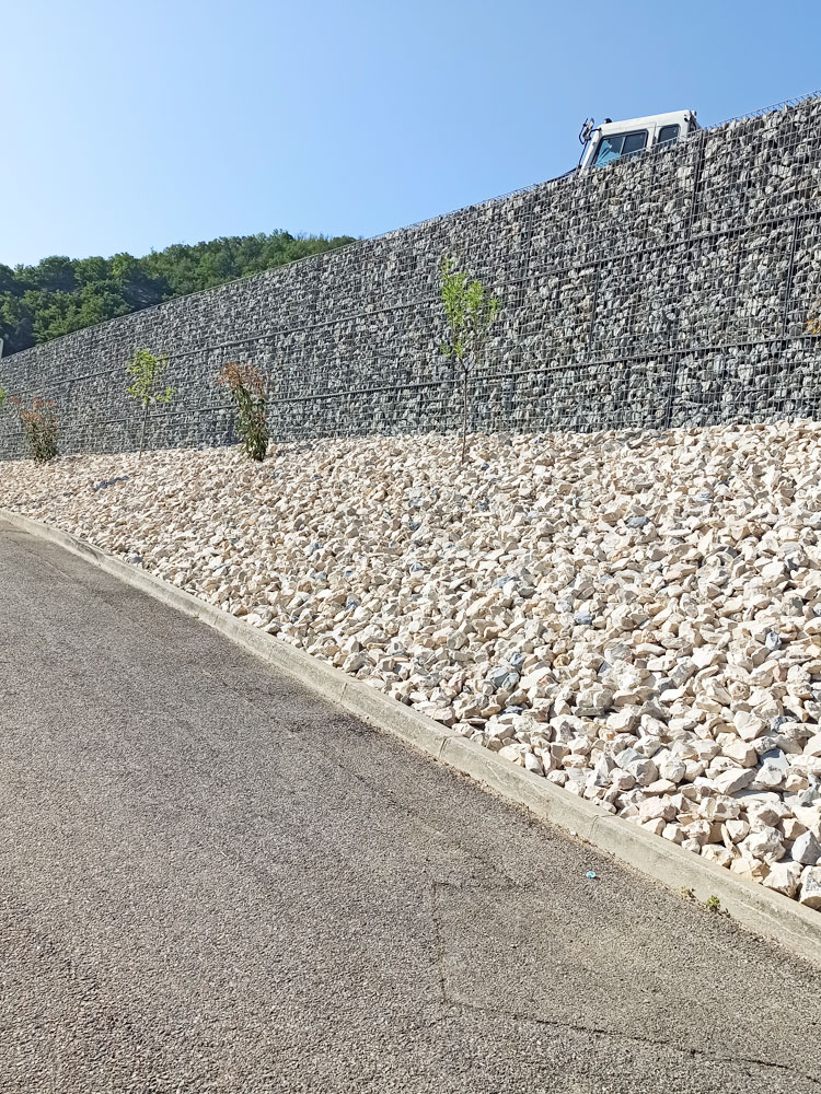 Muro de contenção de grande escala em gabiões Bagston, com talude inferior protegido por agregados decorativos, oferecendo estabilidade e acabamento estético em obras públicas ou privadas.