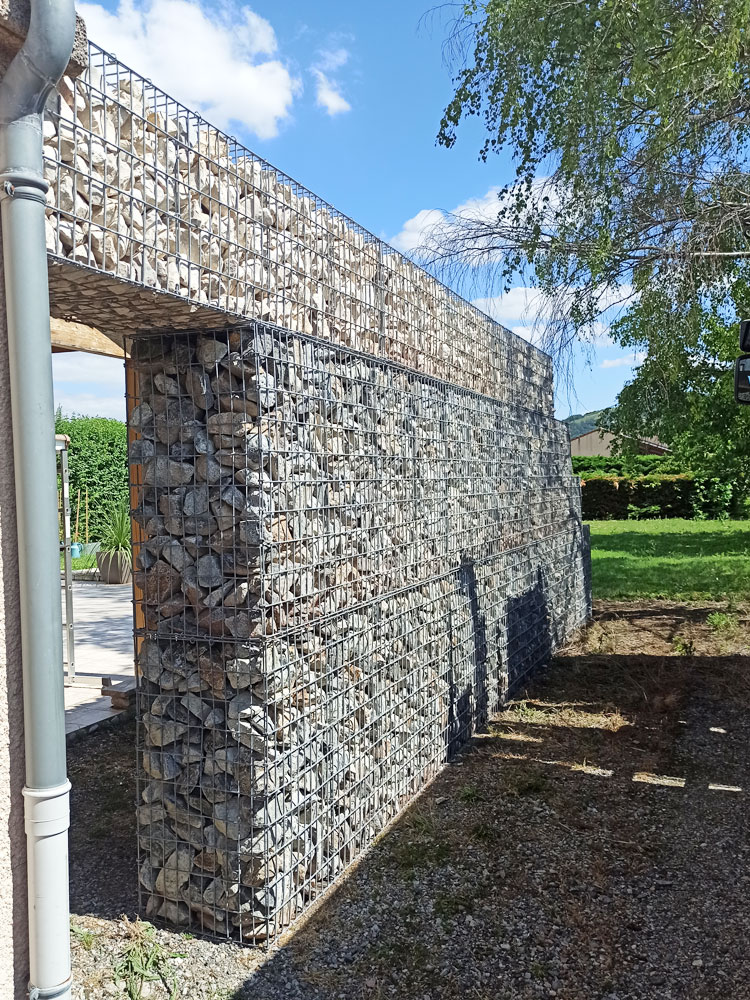 Muro de contenção em gabião com design estrutural que integra uma passagem, combinando resistência técnica com estética decorativa para espaços exteriores.