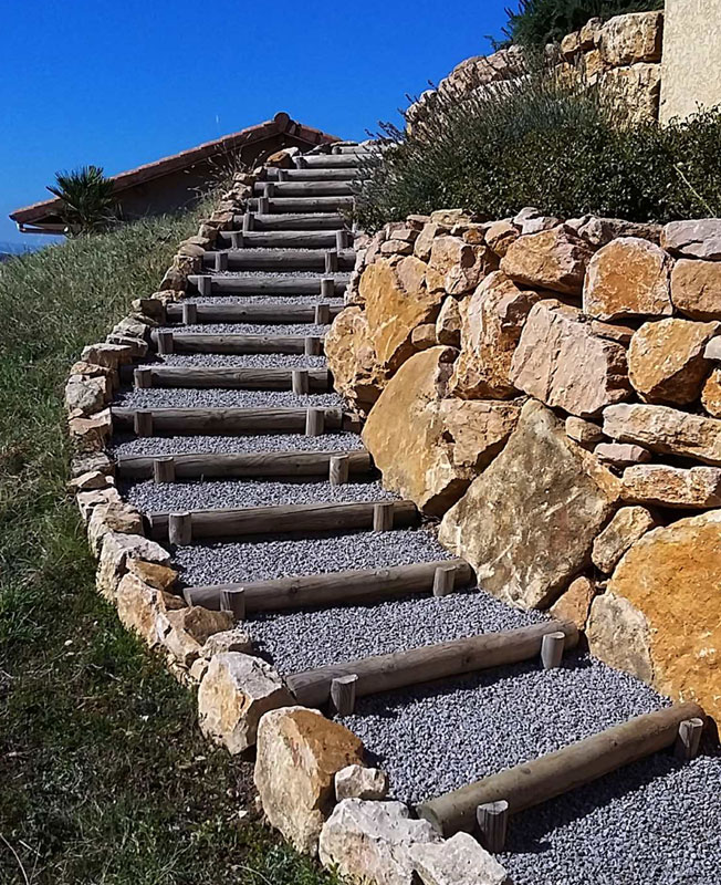 Escadaria exterior estruturada com madeira e preenchida com agregados decorativos, oferecendo um acesso estável e estético em projetos de paisagismo.